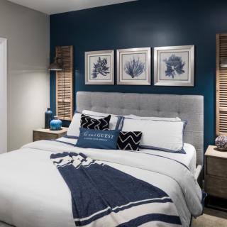 A modern bedroom featuring a blue and white color scheme with decorative pillows and framed wall art.
