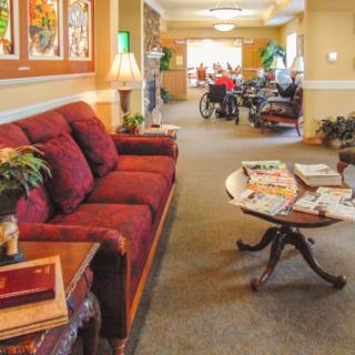 A cozy lobby area with a sofa, table, and magazines, leading to a room with people in the background.