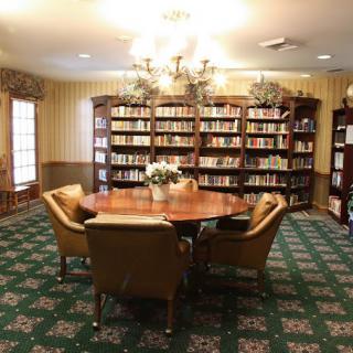A cozy library room with a round table surrounded by chairs and bookshelves filled with books.