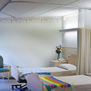 A serene patient room in a medical facility, featuring two beds and a floral arrangement.