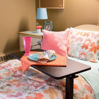 A cozy bedroom setup featuring a floral bedding, a bedside table with a lamp, and a snack tray.