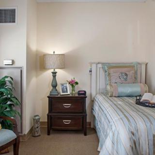 A cozy bedroom with a neatly made bed and a bedside table adorned with a lamp and decorative items.
