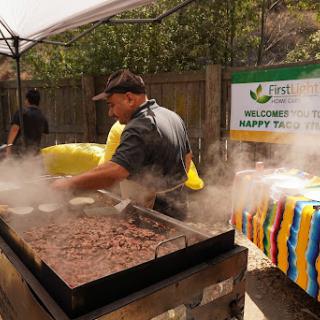 A chef prepares food in a large outdoor cooking setup, surrounded by steam and vibrant decorations for a community event.