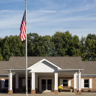 A well-maintained building featuring the United States flag in front, surrounded by a lush landscape.
