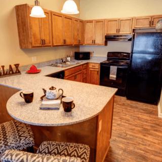 A modern kitchen with wooden cabinets, a black refrigerator and stove, and a cozy breakfast bar with patterned stools.