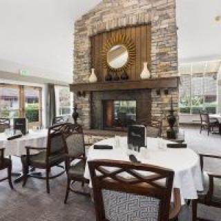 A cozy restaurant dining room featuring a central fireplace, elegantly set tables, and comfortable chairs.