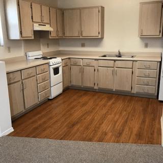 A spacious kitchen with wooden cabinets and flooring, featuring an oven and a sink.