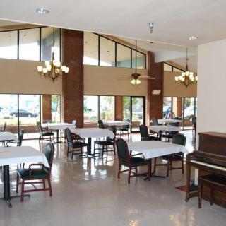 A spacious dining area with tables, chairs, and a piano under elegant chandeliers.