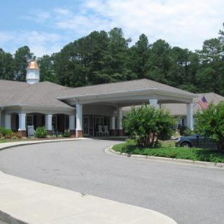 A building entrance with a covered driveway surrounded by trees and landscaping.