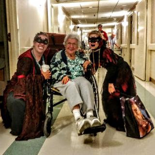 A joyful moment with costumed visitors bringing cheer to a resident in a hospital corridor.
