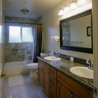 A modern bathroom featuring double sinks, a large mirror, and a bathtub with a shower curtain.