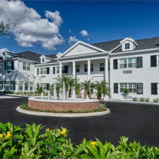 A large residential building with a central fountain and landscaped surroundings under a partly cloudy sky.