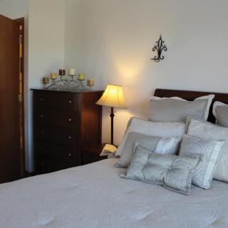 A cozy bedroom featuring a neatly made bed with multiple pillows, a wooden dresser, and a warm lamp.