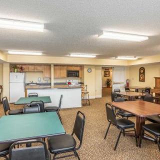 A communal dining area with a kitchen, featuring tables and chairs under bright fluorescent lights.