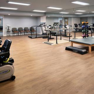 A well-equipped indoor gym with various exercise machines and wooden flooring.