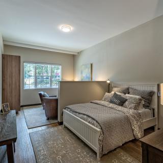 A modern bedroom with neutral tones, featuring a bed and desk near a large window.