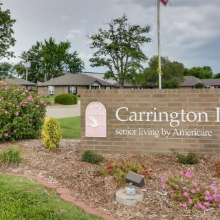 A brick sign for Carrington II, surrounded by landscaping and under a cloudy sky.