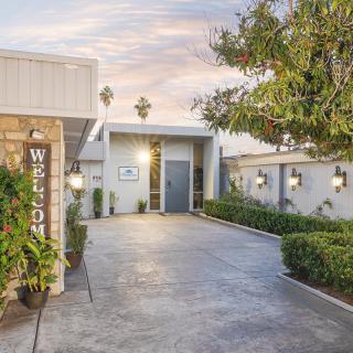 A modern house entrance with a paved driveway, surrounded by well-maintained landscaping and outdoor lights.