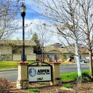 Entrance sign to a residential neighborhood named Aspen, featuring a lamp post and surrounding trees.