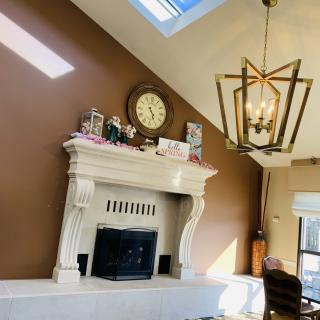 A well-lit living room featuring a decorative fireplace with a clock and ornaments on the mantel, illuminated by natural light from above.