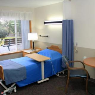 A hospital room with a bed, table, and chair overlooking a window with a scenic view.