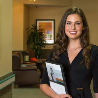 A professional woman smiling in an office environment, holding a folder.