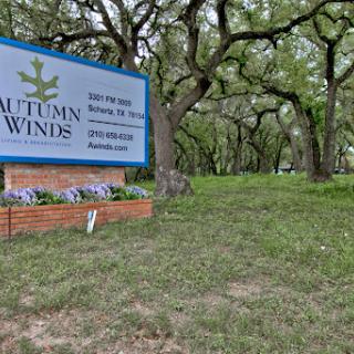 A welcoming sign for Autumn Winds, surrounded by lush greenery and trees.