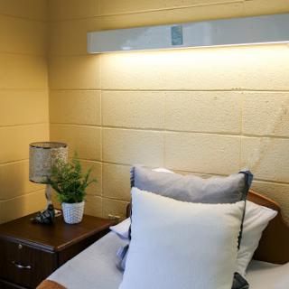 A cozy bedroom corner featuring a neatly made bed with decorative pillows, a stylish nightstand with a lamp, and a small plant.