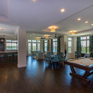 A spacious and modern living area featuring a pool table, elegant furnishings, and ample natural light streaming through large windows.