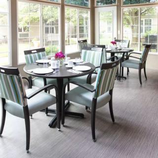 A bright and modern dining room with neatly arranged tables and chairs, surrounded by large windows.
