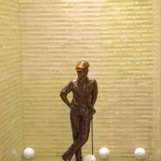 A bronze statue of a person leaning with a cane, showcased in a display case.