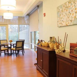 A well-lit dining room with a table and chairs, featuring large windows and decorative elements on a sideboard.