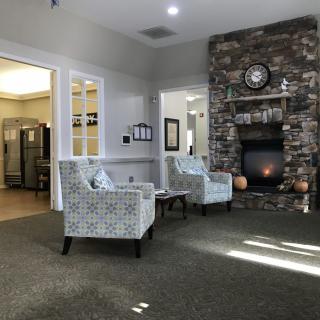 A cozy living room featuring a stone fireplace, two patterned chairs, and a clock on the mantel.