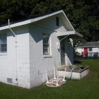A small white house with a porch and grassy yard, showcasing a simple rural lifestyle.
