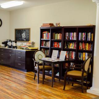 A cozy library corner with bookshelves, a small table with chairs, and a coffee station on a wooden floor.