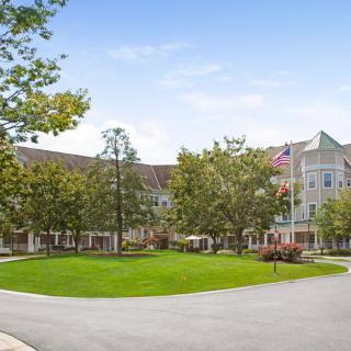 A scenic view of a large building surrounded by trees and a grassy area under a clear blue sky.