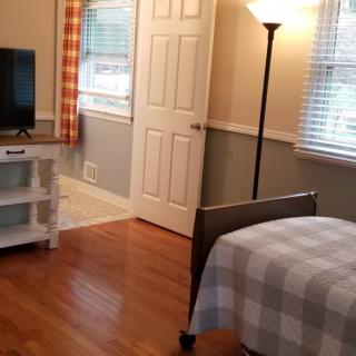 A cozy bedroom with a bed, lamp, and television on a hardwood floor.