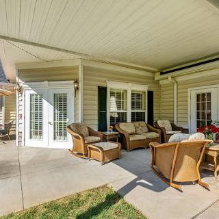 A cozy patio with wicker chairs and a sofa under a covered porch, accessed through French doors on a sunny day.