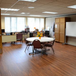 A well-lit office meeting room featuring a round table and chairs, suitable for group discussions.