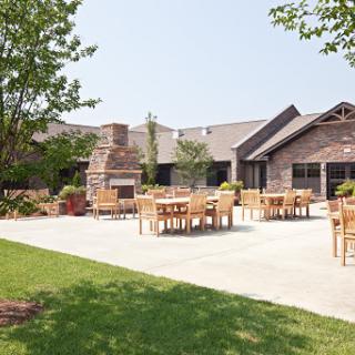 A sunny outdoor patio area with tables and chairs, surrounded by well-maintained grass and landscaping.