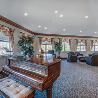 A spacious and elegantly furnished living room with a grand piano, comfortable seating, and large windows allowing natural light.
