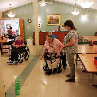 A caregiver assists a resident in a wheelchair during an indoor activity in a senior care facility.