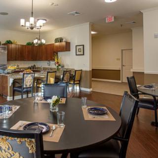 A modern dining area with a kitchen in the background, featuring neatly set tables and elegant lighting.