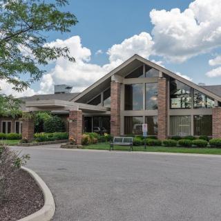A modern building with large glass windows and a landscaped entrance under a cloudy sky.