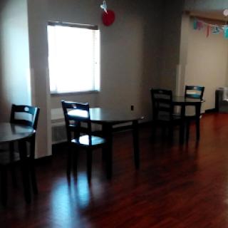 A quiet interior scene featuring several empty tables and chairs, with a window letting in natural light.
