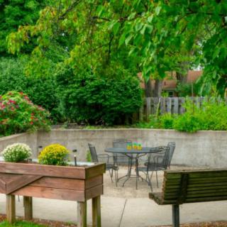 A serene garden patio with a table, chairs, and lush greenery.
