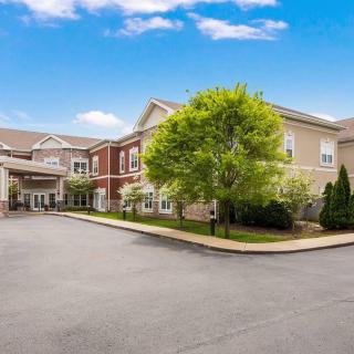 A hotel exterior with a parking area and surrounding trees on a clear day.