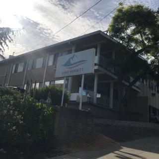 A two-story building with a sign out front, surrounded by greenery under a partially cloudy sky.