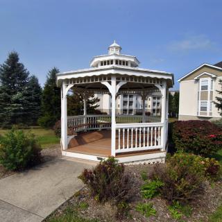 A charming gazebo situated in a garden area with surrounding greenery and a house nearby.