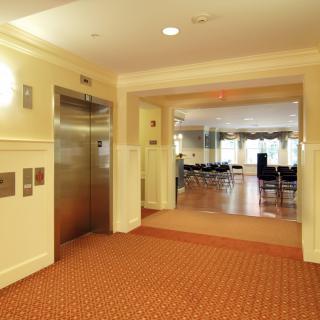 A well-lit hallway in a building, featuring an elevator and an adjoining room.